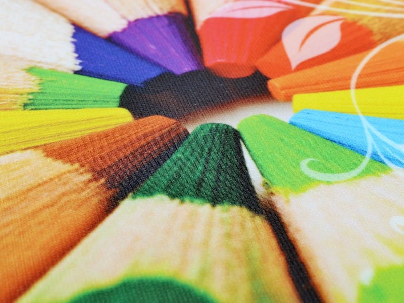 Close-up van bedrukt decotex-textiel: kleurpotloden in volle kleur op de fijne weefstructuur