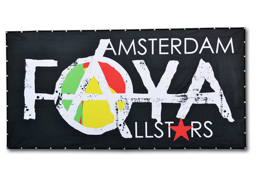 Zwart heavytex-doek met een grote witte bandnaam en een rood-geel-groen accent