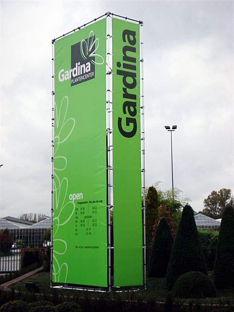 Hoge driezijdige totem met groene spandoeken in een buisframe bij een tuincentrum