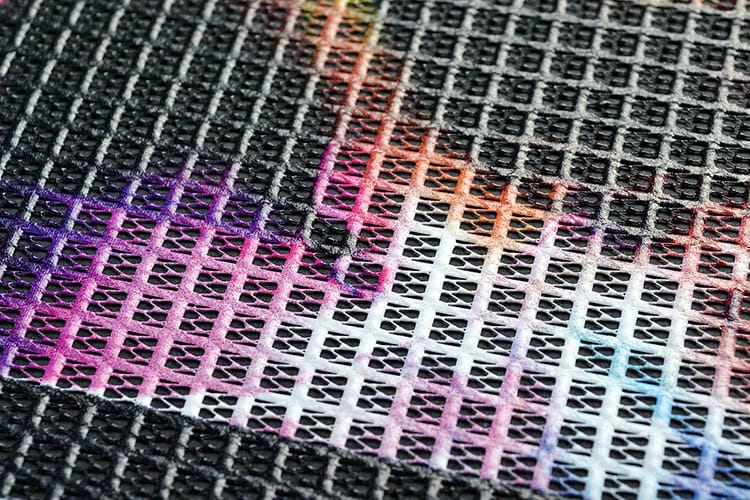 Close-up van speaker-mesh: volle kleur op een grof, open weefsel