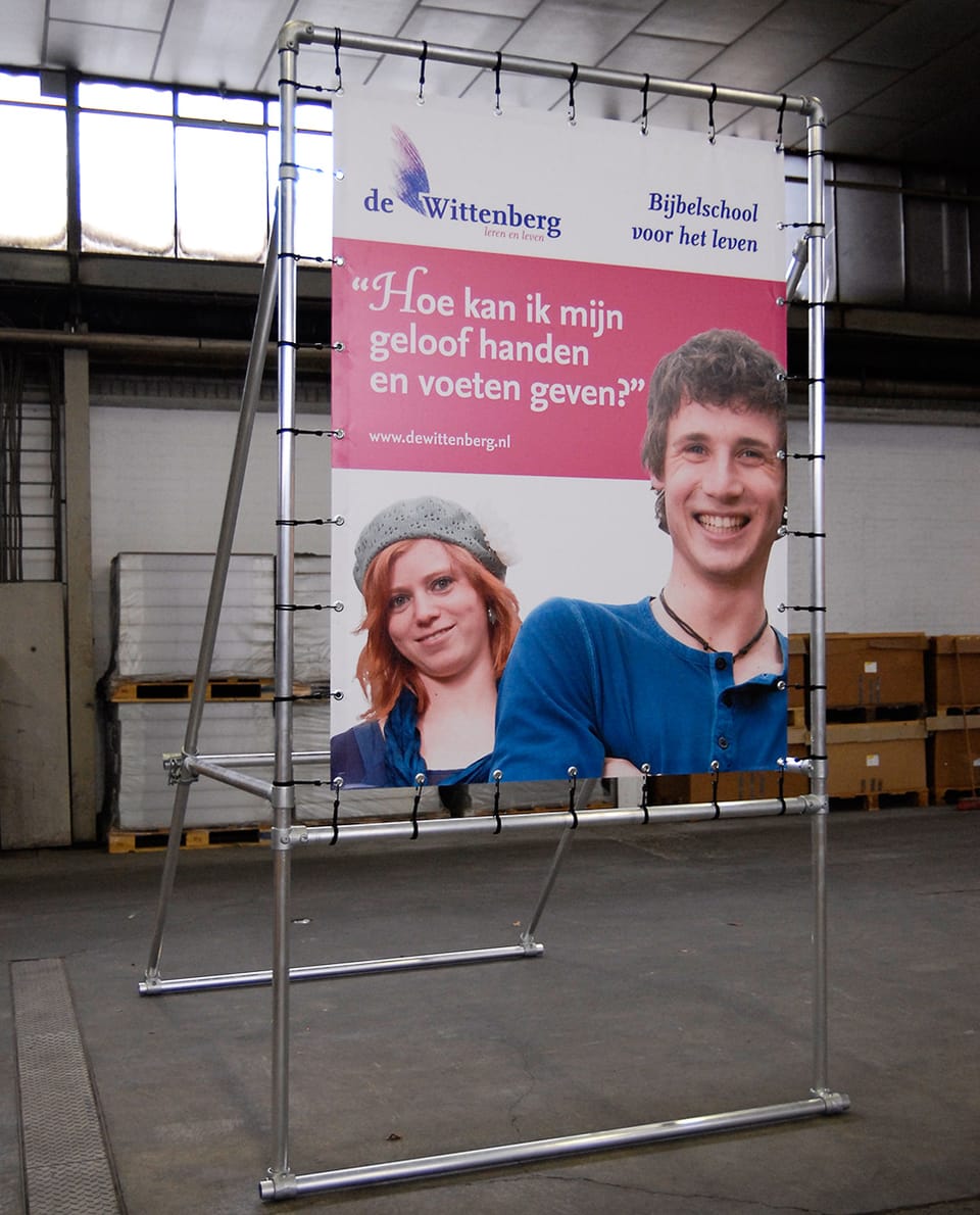 Spandoek met twee portretten en een citaat in een vrijstaand buisframe in een magazijn