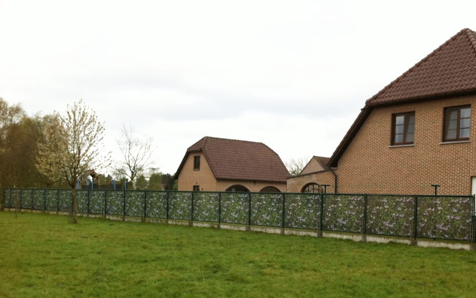 Bedrukt meshdoek als lange tuinafscheiding langs een grasveld bij woonhuizen