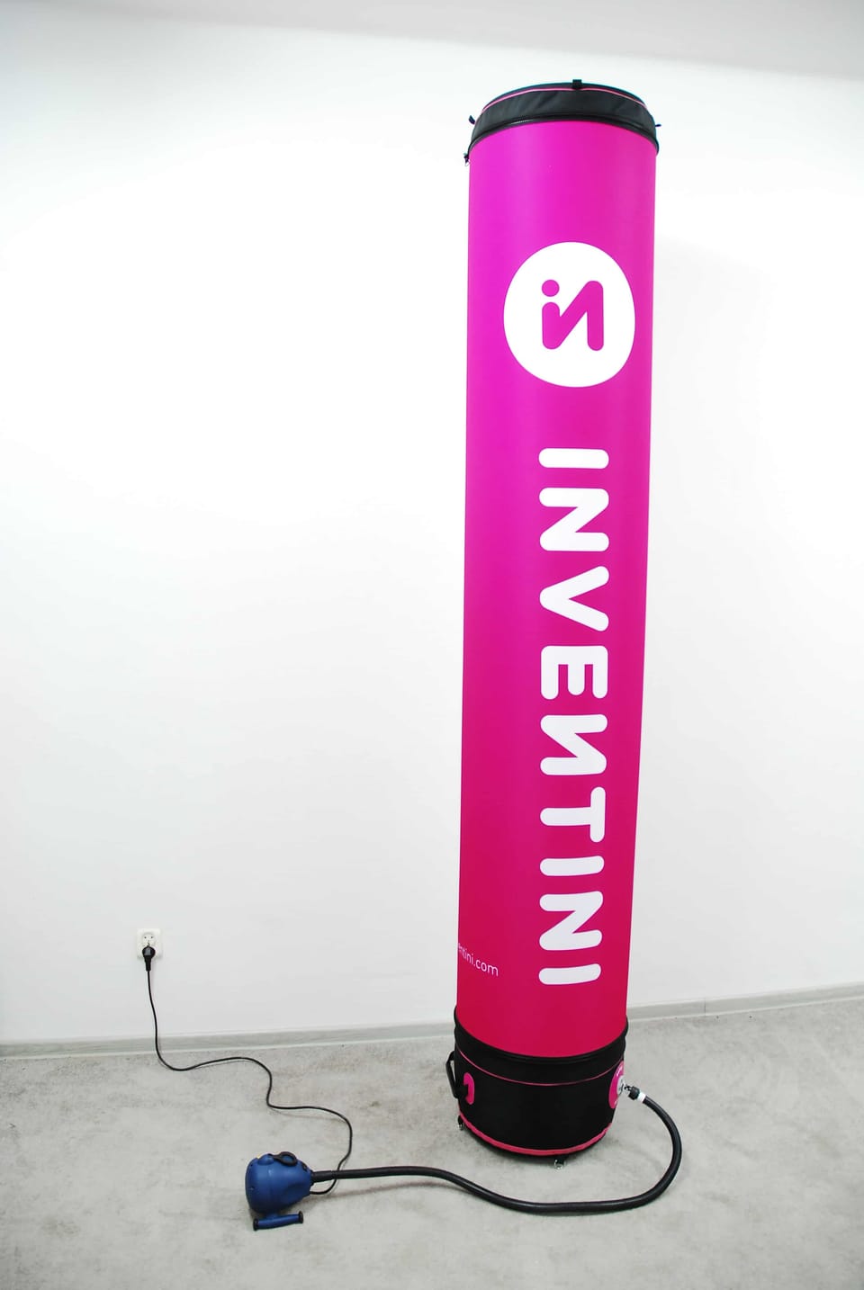 Opblaasbare roze reclamezuil met logo, aangesloten op een pompje in een lege ruimte