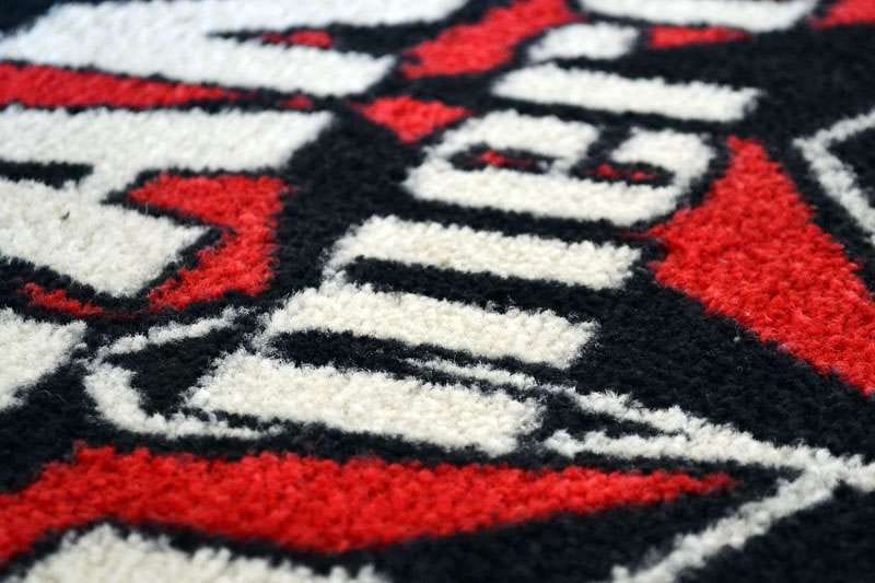 Detail van een getuft logo in rood, wit en zwart in hoogpolig tapijt