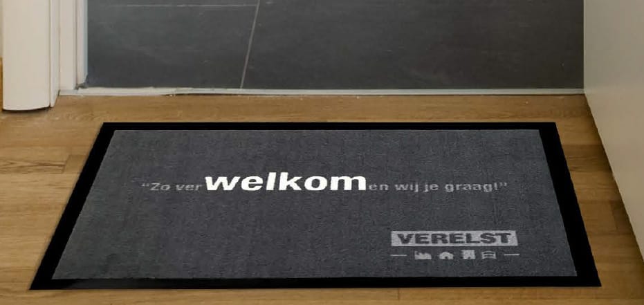 Grijze deurmat met welkomsttekst en logo in een hal