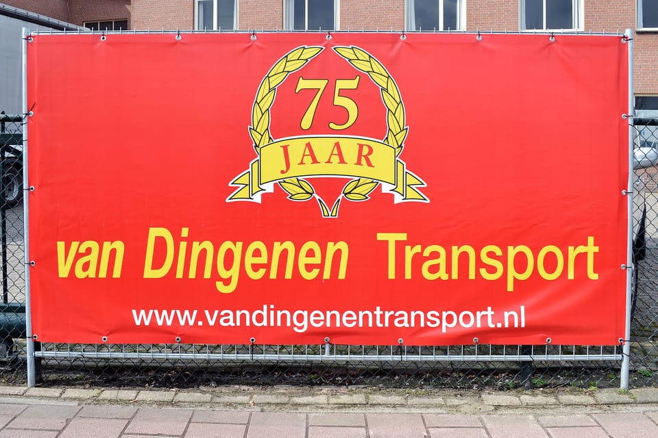 Rood spandoek met jubileumlogo strak gespannen op een hekwerk langs de stoep