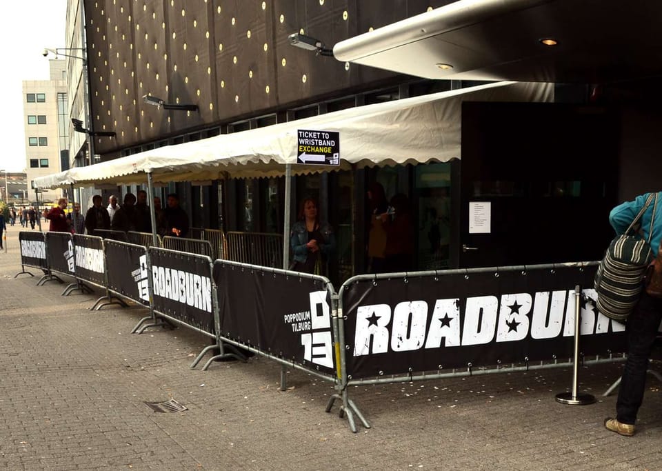 Zwarte dranghekbanners met bandnaam langs de ingang van een poppodium