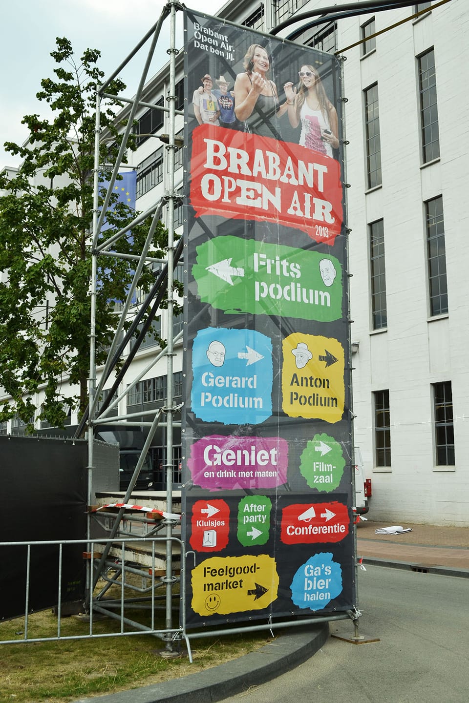 Hoog meshdoek met podiumwegwijzers aan een steigerframe op een festivalterrein